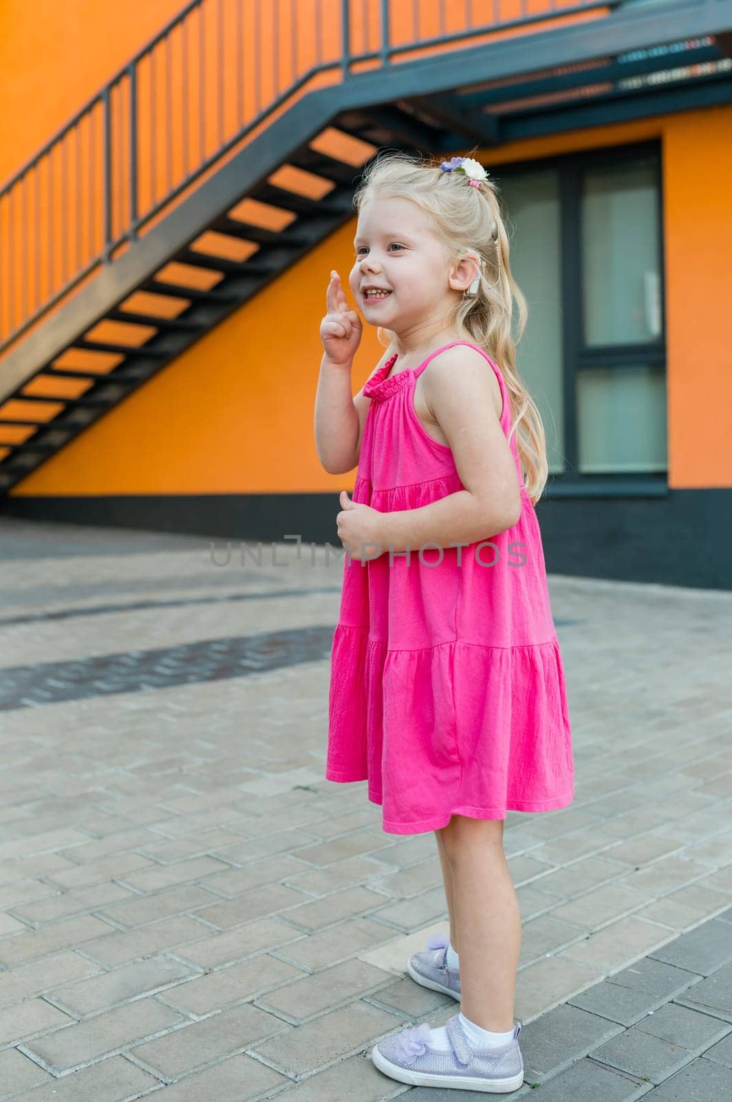 Child girl walks and have fun outdoor with cochlear implant on the head. Hearing aid and treatment concept. Copy space vertical.