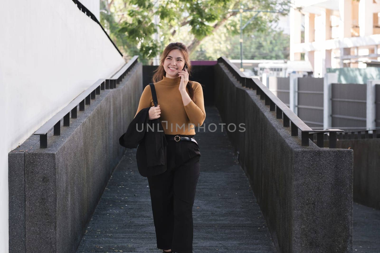 A woman is talking on her cell phone while walking down a stairway. She is wearing a brown sweater and black pants