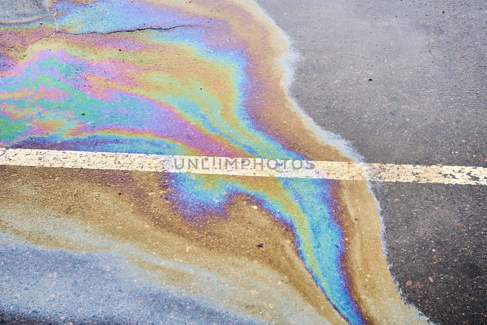 Oil spillage on wet pavement, parking lot with dividing lines, underscoring the environmental obstacles tied to water pollution.