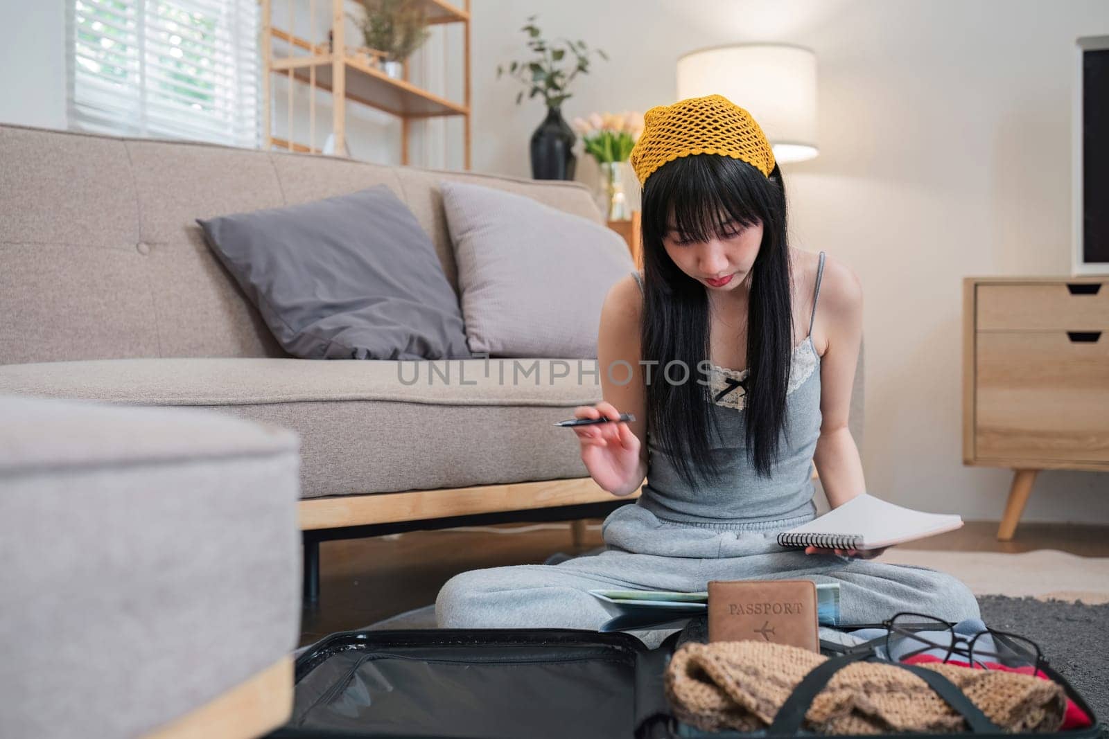 A woman sits on the floor with a passport and a pen in front of her. She is planning to go on holiday..