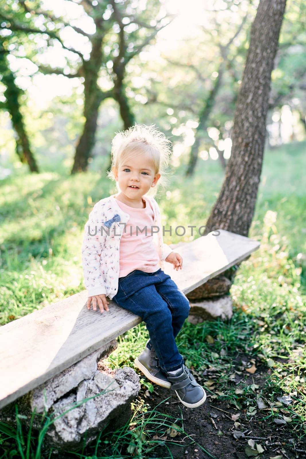 Little smiling girl sitting on a bench in the forest. High quality photo