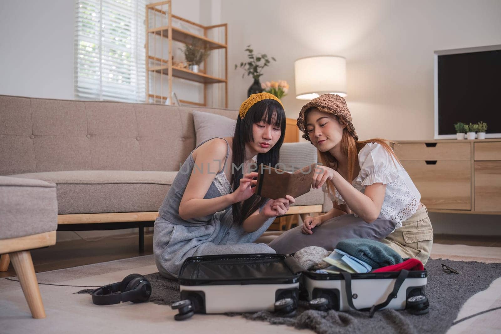 Two women sitting on the floor with suitcases Both of them were checking their passports. They are planning to go on vacation. by wichayada