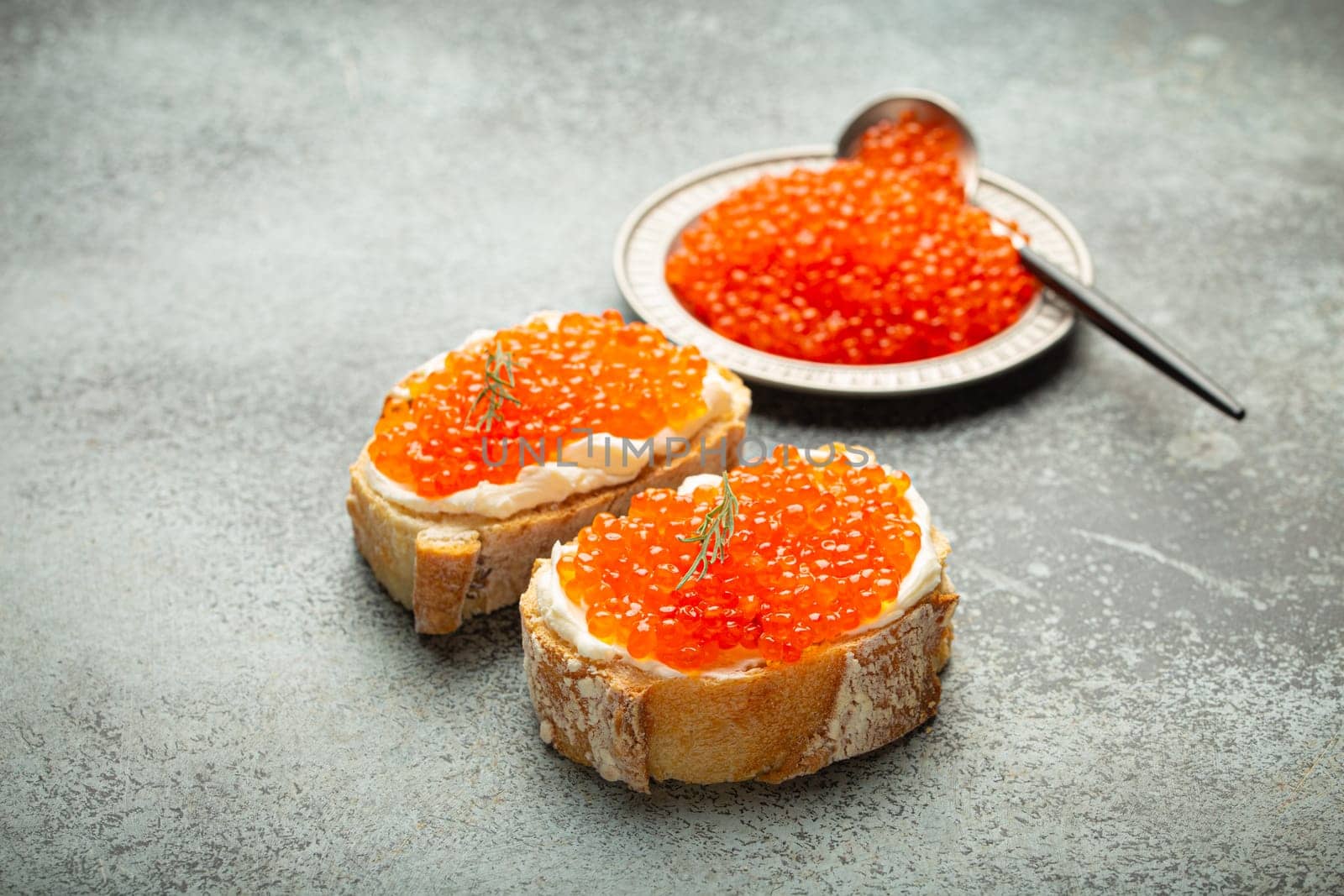 Small metal plate with red salmon caviar and two caviar toasts canape on grey concrete background, festive luxury delicacy and appetizer by its_al_dente