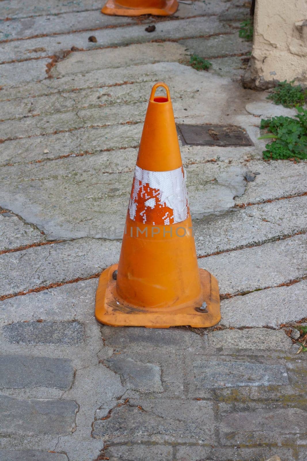 This battered orange traffic cone stands as a weathered symbol of the wear and tear endured on the roads, serving as a reminder of safety measures and road maintenance