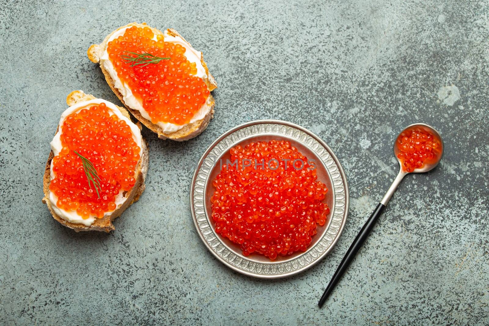 Small metal plate with red salmon caviar and two caviar toasts canape top view on grey concrete background, festive luxury delicacy and appetizer.