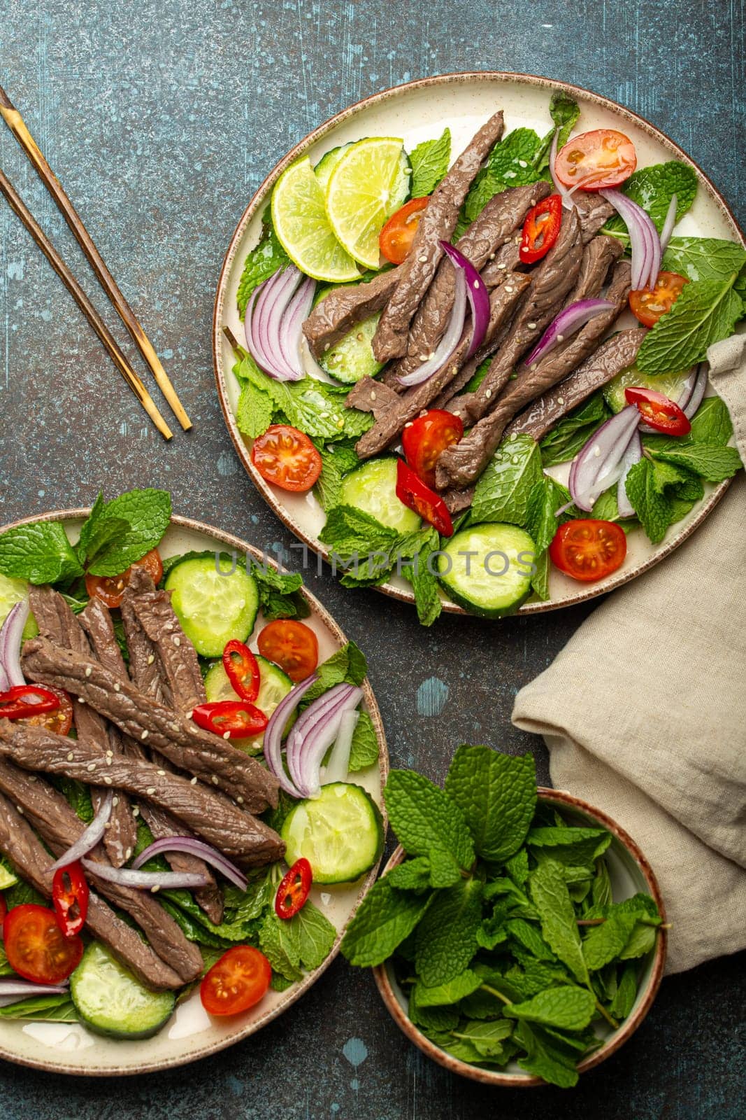 Two plates with traditional Thai beef salad with vegetables and mint top view served on rustic concrete background, healthy exotic asian meal by its_al_dente