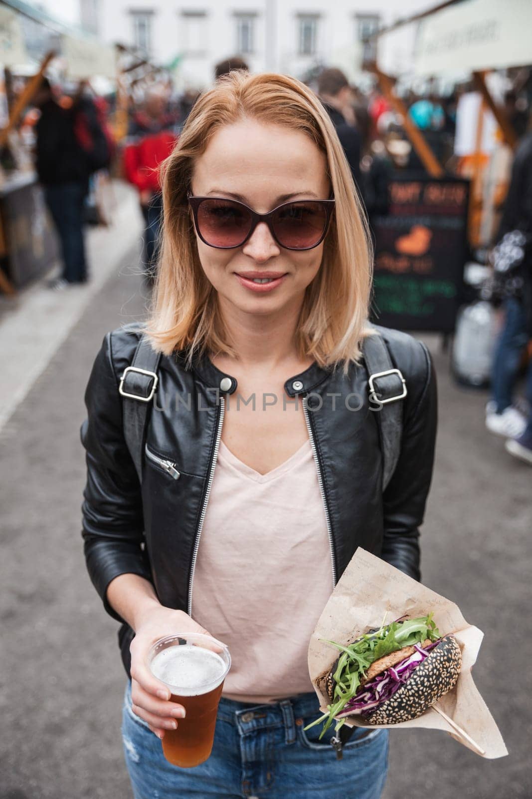 Beautiful young woman holding delicious organic salmon vegetarian burger and homebrewed IPA beer on open air beer an burger urban street food festival in Ljubljana, Slovenia. by kasto