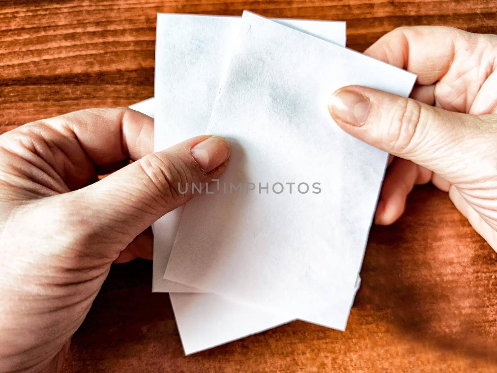 Woman Holding Small White Papers Over a Wooden Surface. Hands presenting several small white papers by keleny