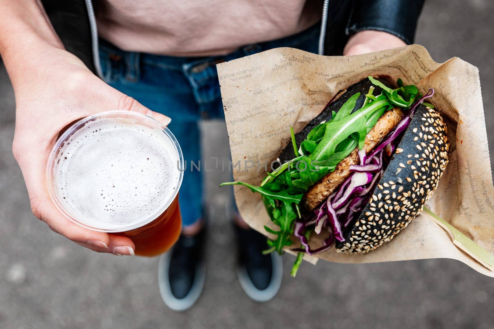 Close up of woman hands holding delicious organic salmon vegetarian burger and homebrewed IPA beer on open air beer an burger urban street food festival in Ljubljana, Slovenia. by kasto