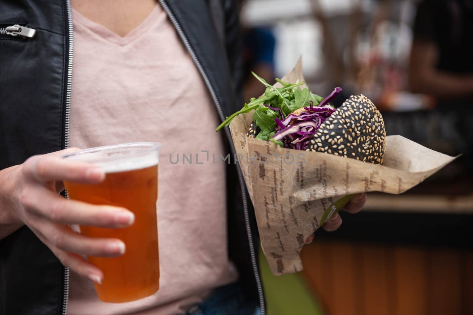 Close up of woman hands holding delicious organic salmon vegetarian burger and homebrewed IPA beer on open air beer an burger urban street food festival in Ljubljana, Slovenia. by kasto