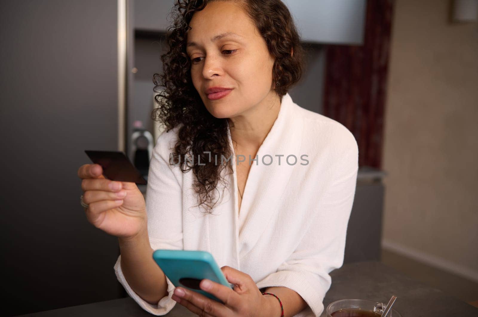 Attractive woman at home holding black credit card and smartphone, booking hotel, ordering food, transferring money via internet banking, making payment, using mobile app. Copy advertising space by artgf