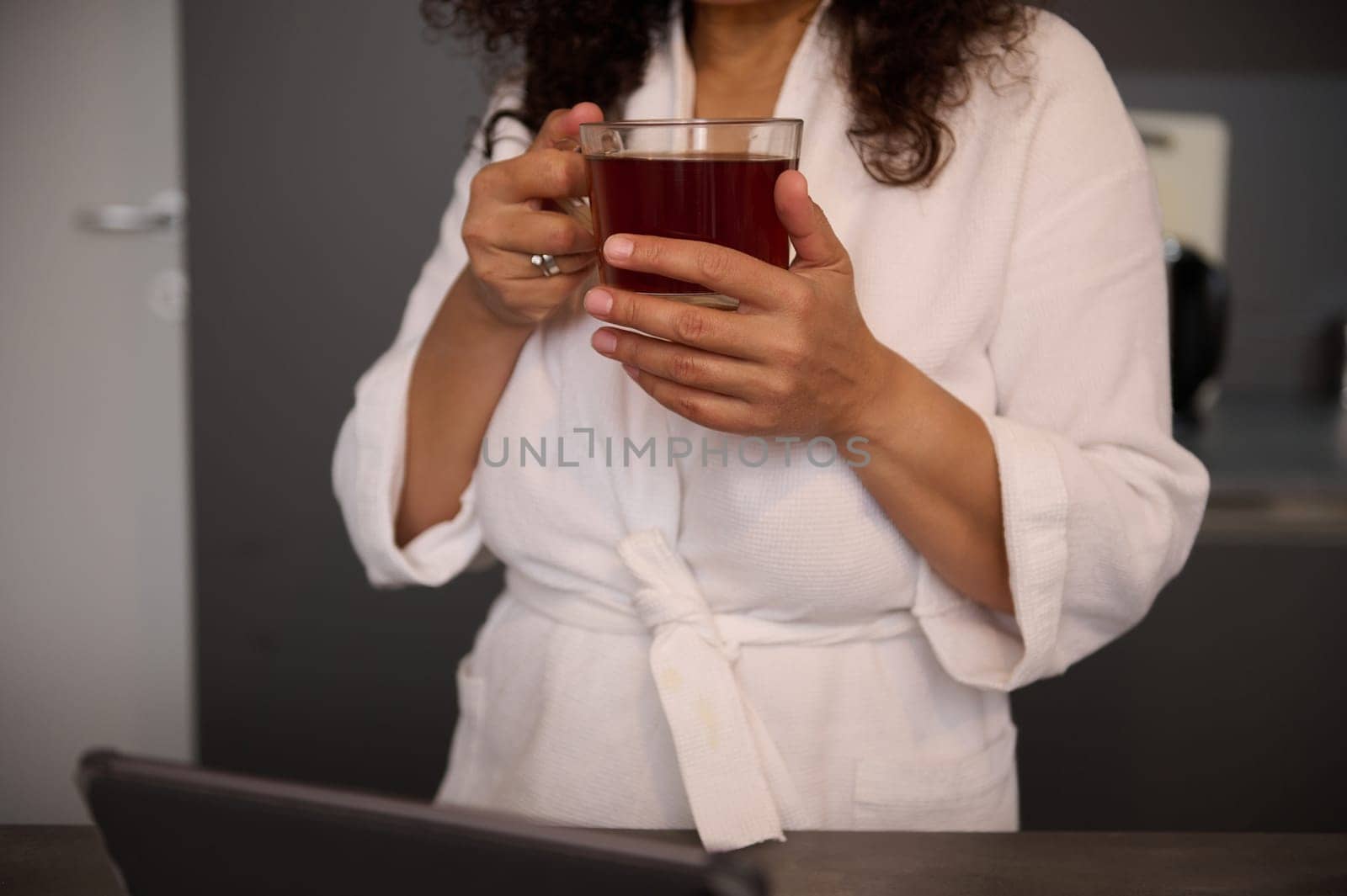 Cropped view of hands of woman in white bathrobe, holding a cup of hot tea