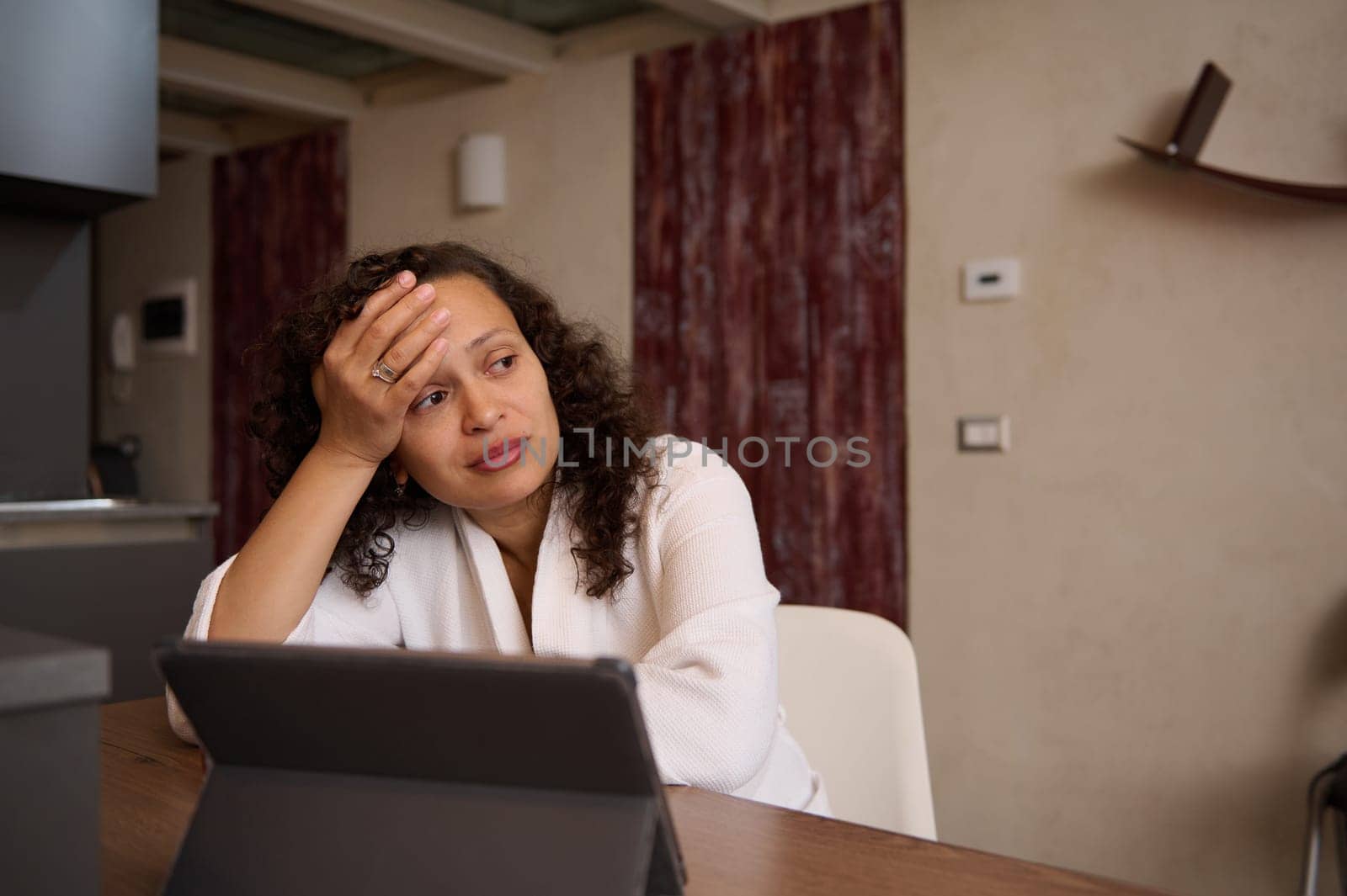 Overworked young freelance woman feeling headache after computer work, suffering from fatigue, looking away, sitting at kitchen table, telecommuting from home office in her weekend. People. Online job