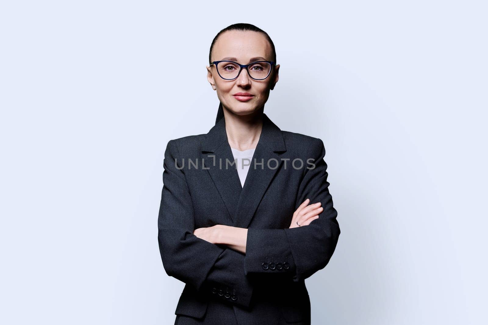 Portrait of business woman in 30s with crossed arms, on white studio background. Confident female in glasses, suit looking at camera. Business, work, job, career, people concept