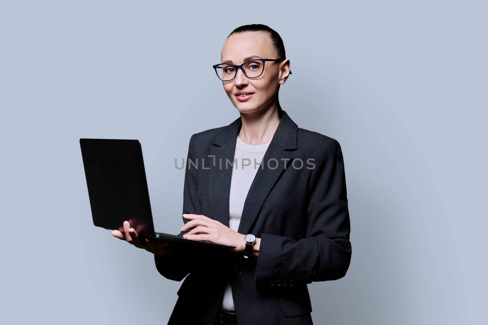 Middle-aged business confident woman using laptop on gray background by VH-studio