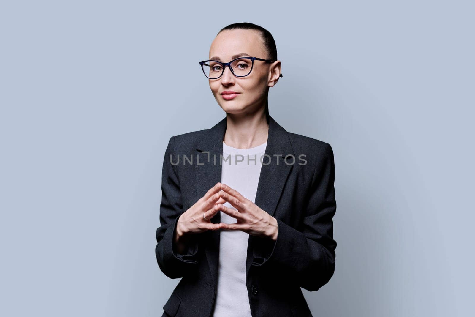 Portrait of thinking serious 30s business woman on grey studio background. Confident female in glasses, suit looking at camera. Business work teaching job career people concept