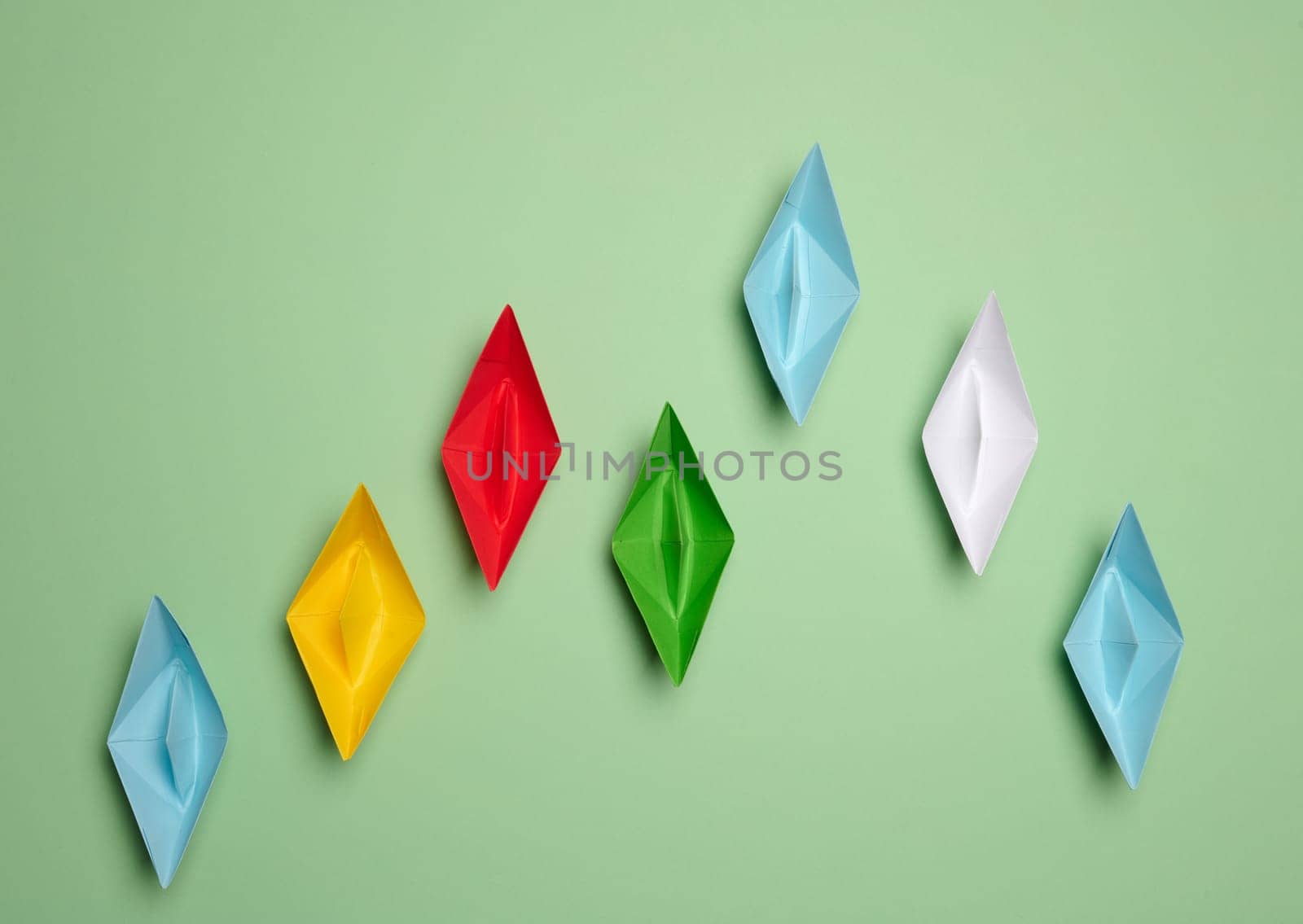 Multi-colored paper boats move forward, some of them rush forward. Concept of rivalry by ndanko