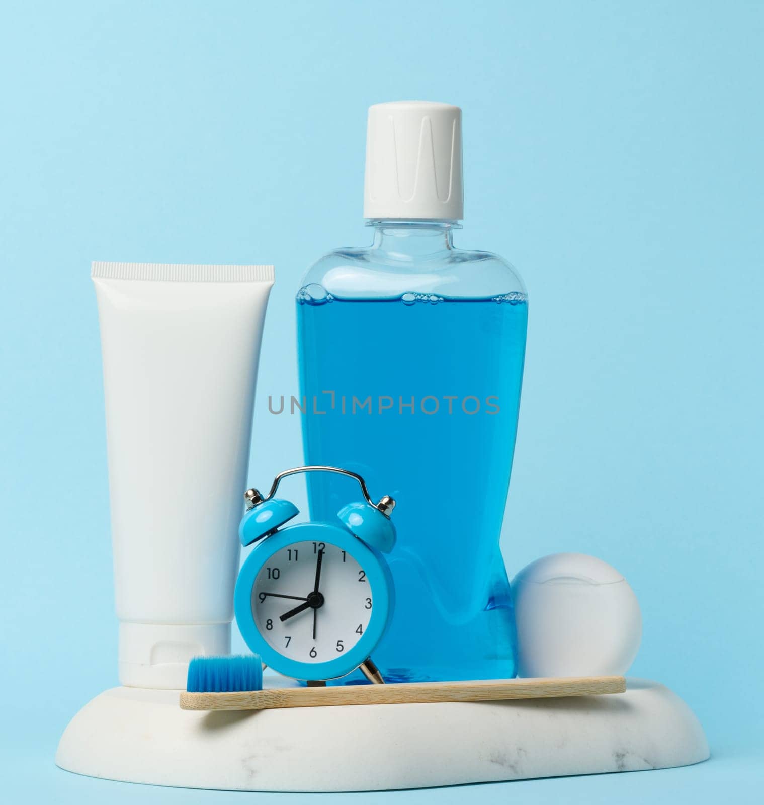 Mouthwash and toothpaste tube, alarm clock on blue background, oral hygiene by ndanko