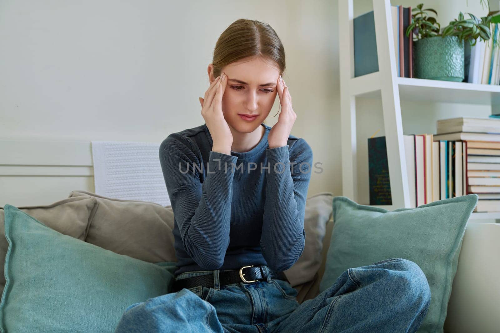 Young suffering teenage female having headache, holding head with hands, sitting on couch at home. Health, problems, mental difficulties, depression, youth concept