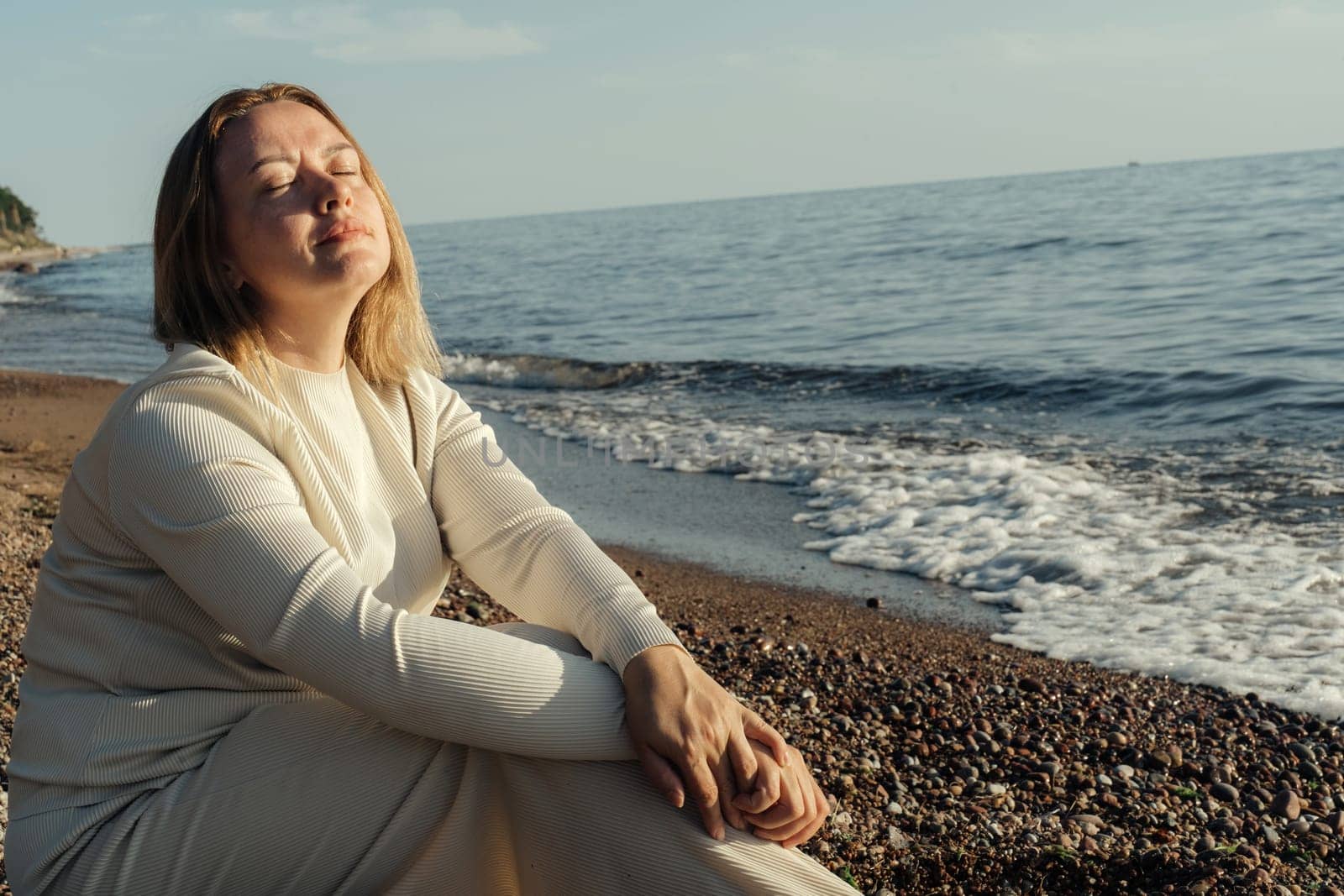 A woman sitting on the sandy beach, gazing out towards the vast ocean in contemplation and relaxation.