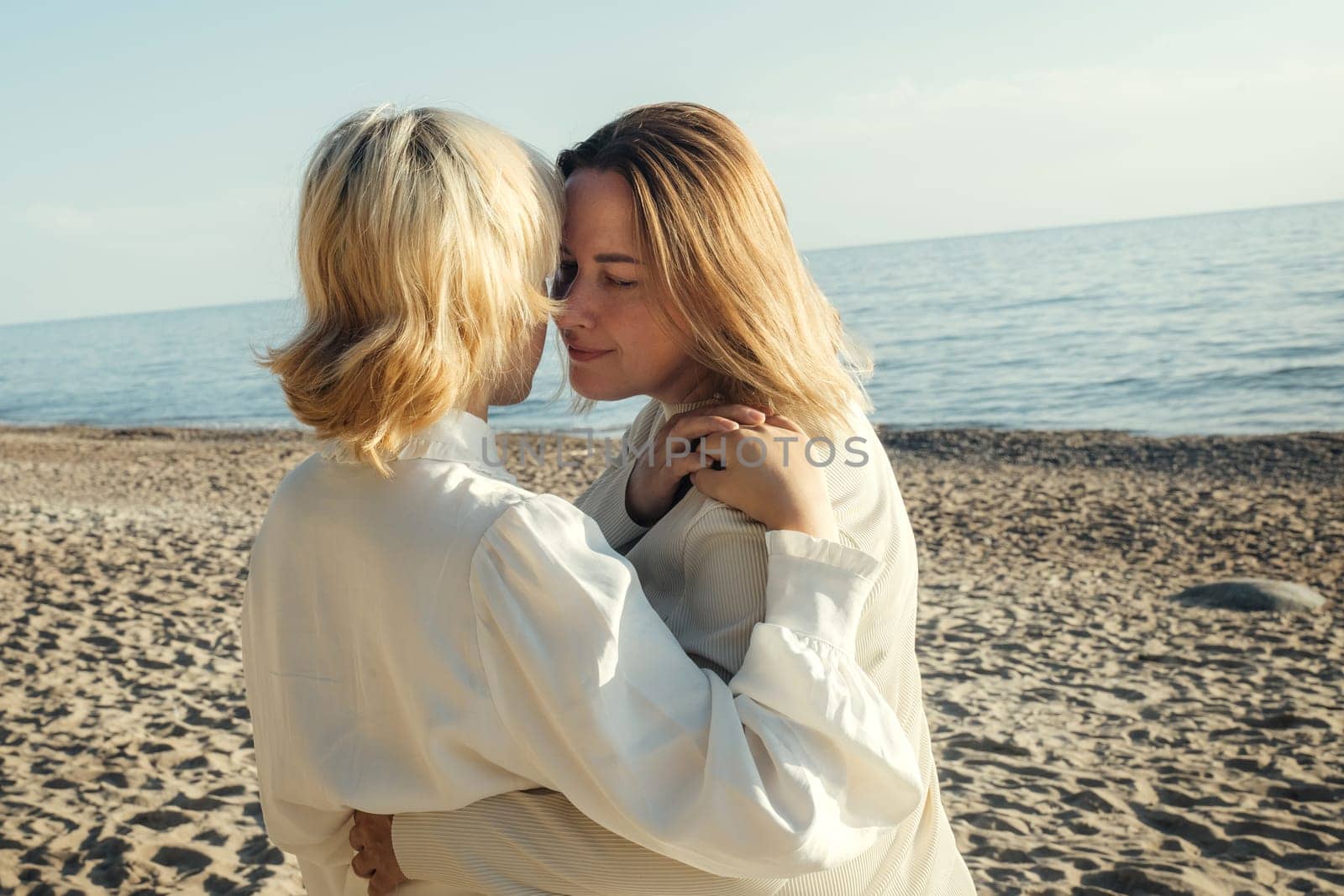 Mom and daughter are standing on the beach by the sea, hugging.