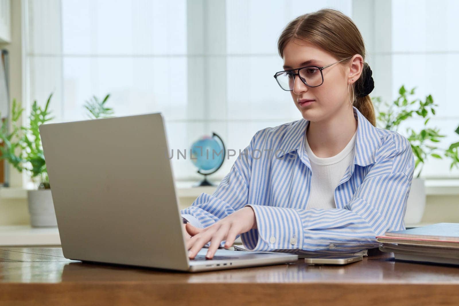 Young smiling girl typing on laptop computer at home. Female freelancer working remotely, high school, college student studying online preparing for exams. Technology youth training education work