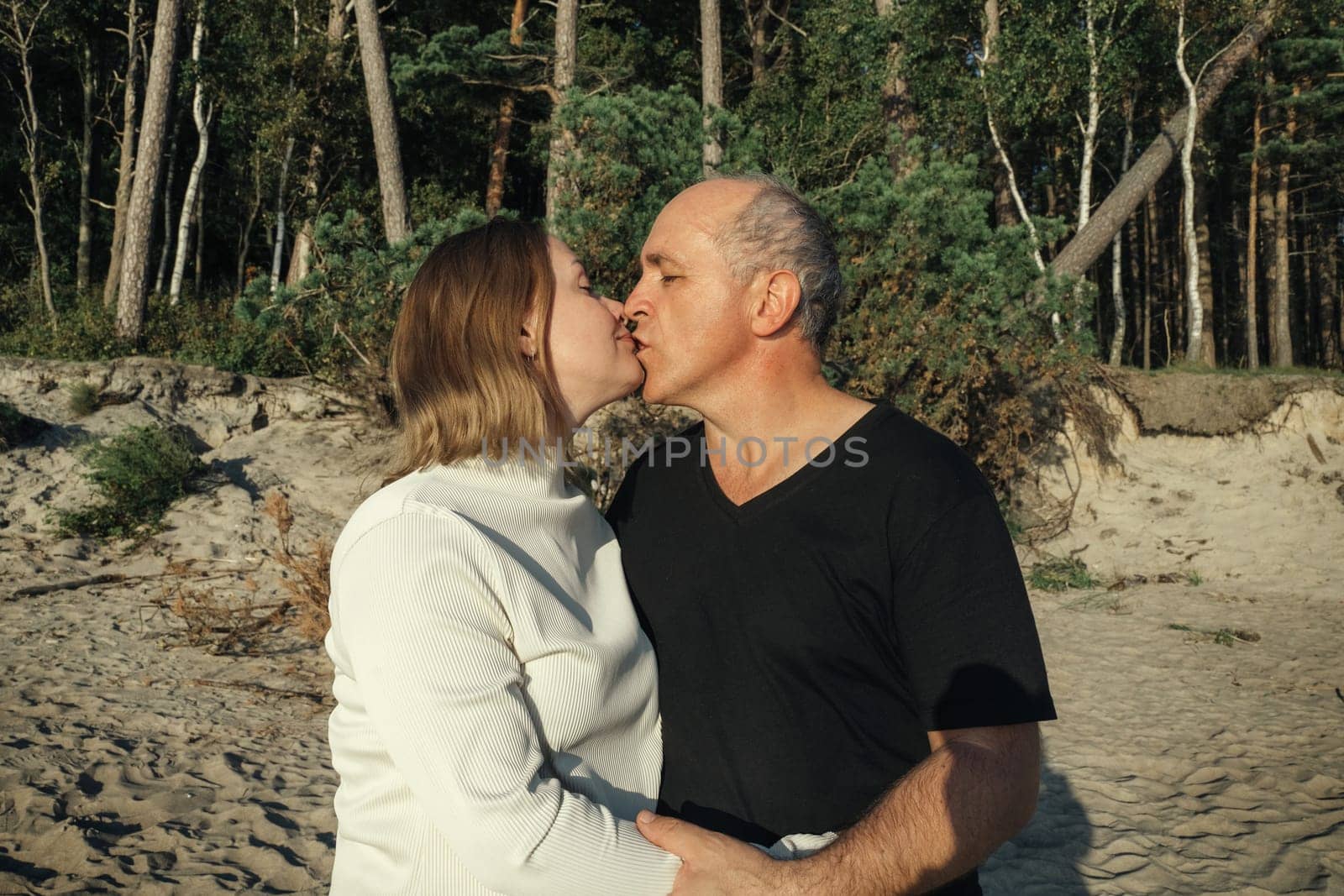 A man and a woman romantically kissing on the sandy beach with the ocean waves in the background.