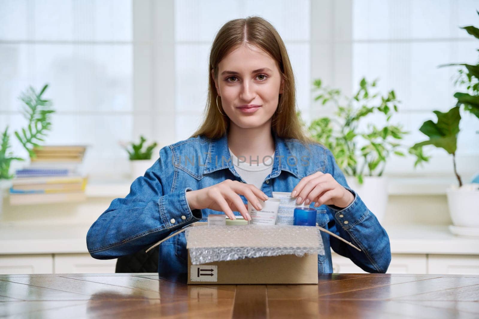 Satisfied young female customer buyer sitting at home unpacking cardboard box with online purchases. Teenage girl unpacking boxes with cosmetics care products perfumes. Delivery by mail, online store