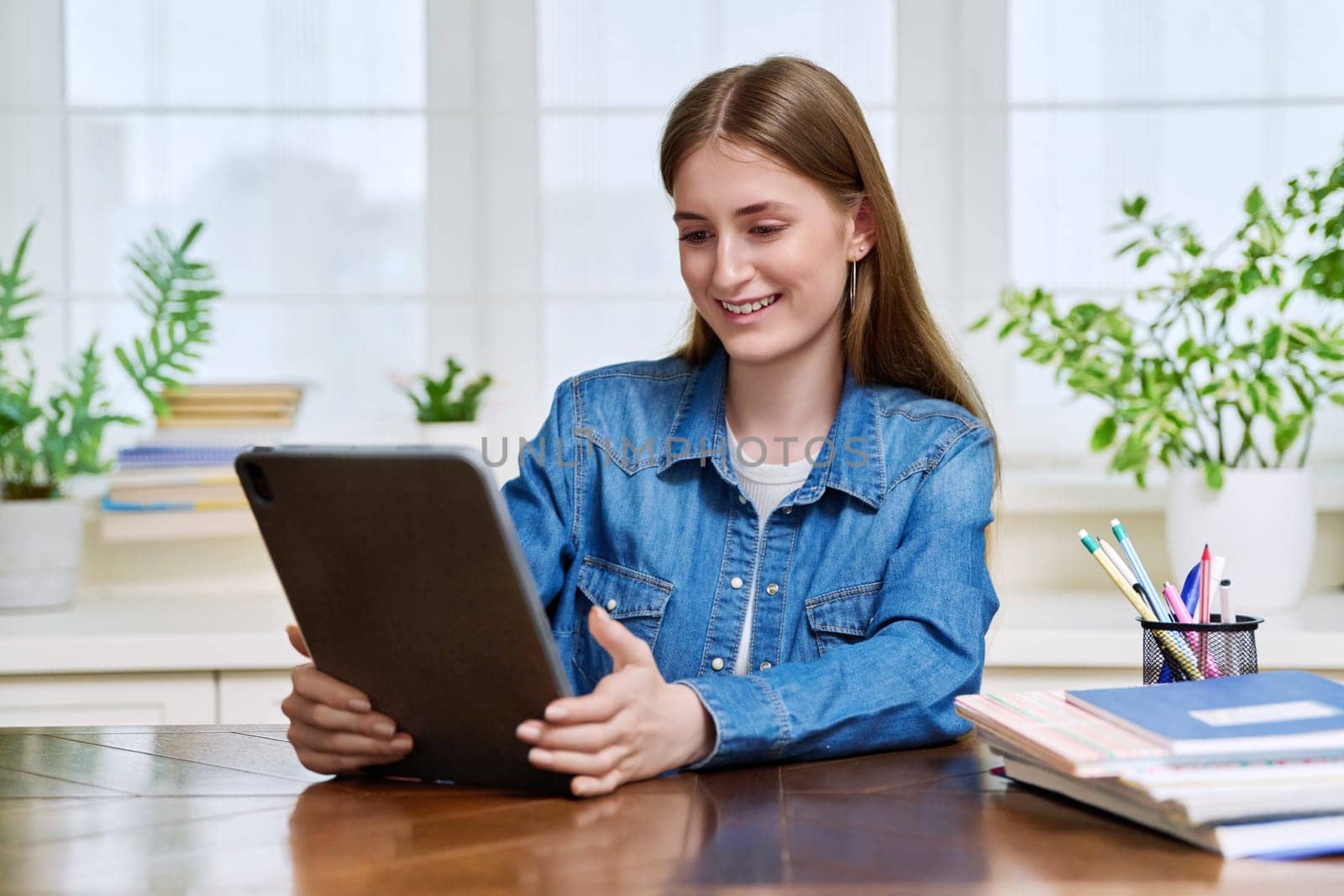 Young teenage female student sitting at home looking talking in web camera of digital tablet. Girl teenager 16,17,18 years old studying remotely, video conference call, e-learning technology education