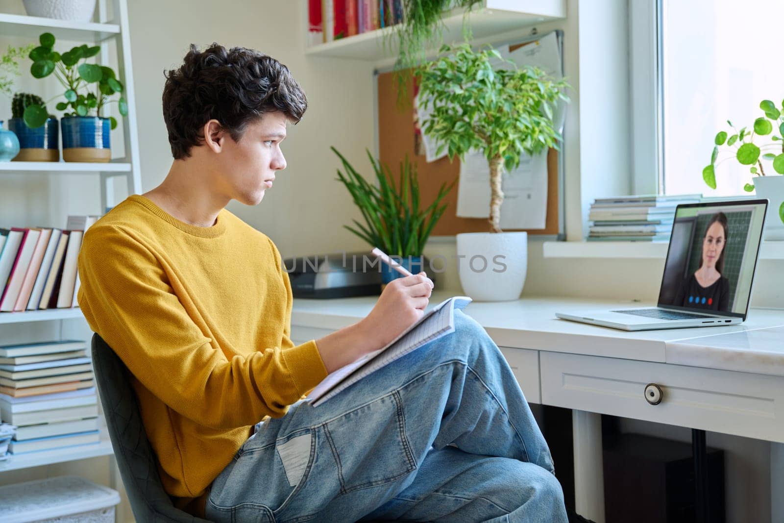 Guy college student sitting at home, looking at laptop screen, making notes in notebook by VH-studio