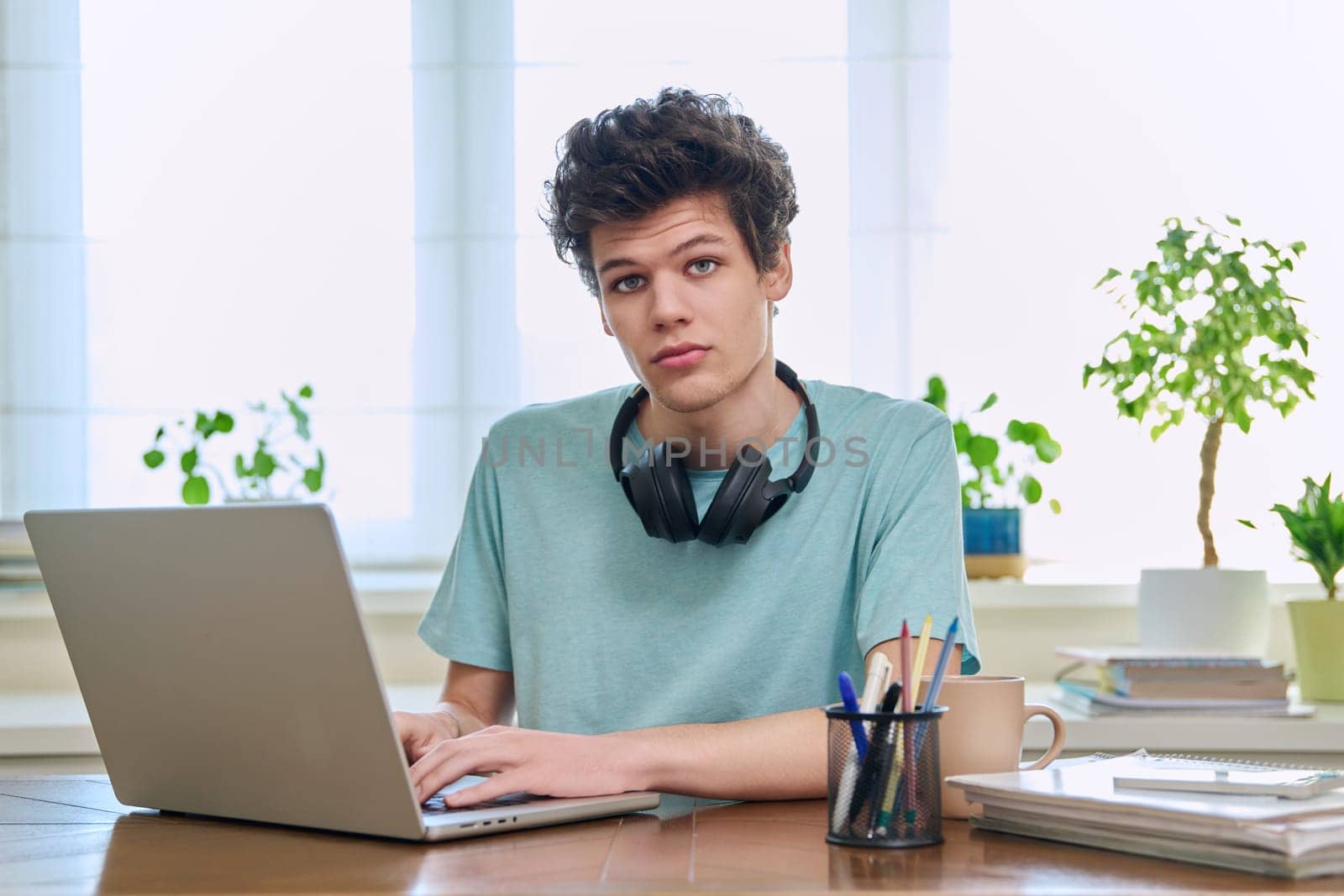 Young male college student sitting at desk with laptop looking at camera by VH-studio