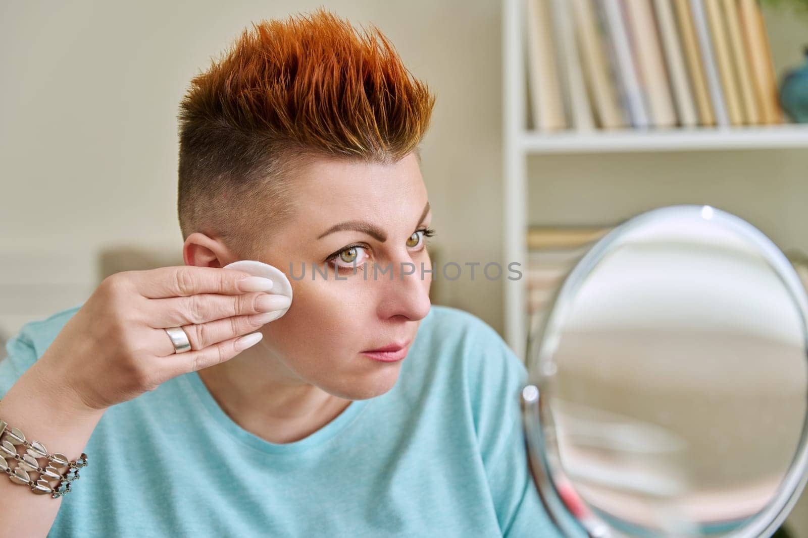 Middle-aged woman with a mirror taking care of her facial skin by VH-studio