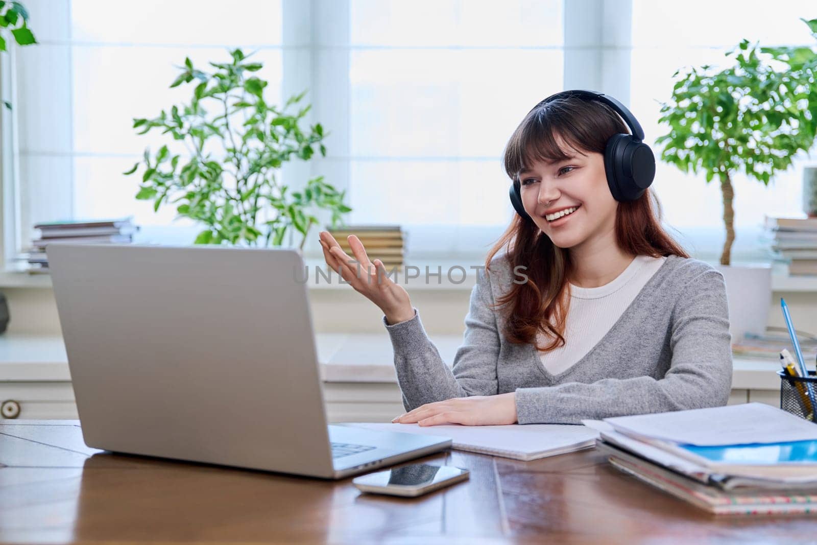 Teenage girl college student in headphones having video conference chat online meeting lesson webinar on computer laptop screen, sitting at desk at home. E-learning, education, technology, knowledge