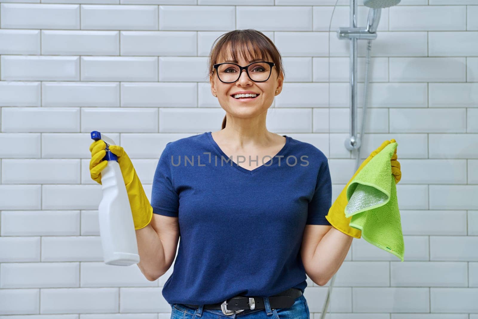 Woman in gloves with detergent spray washcloth doing cleaning in bathroom by VH-studio