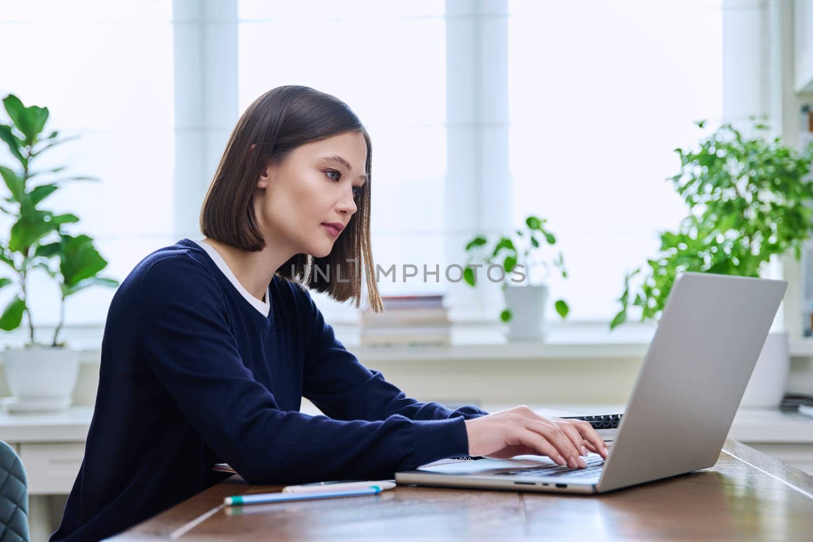 Young female using computer laptop for studying, working, serious young woman typing on keyboard. Technology, education, training, youth concept