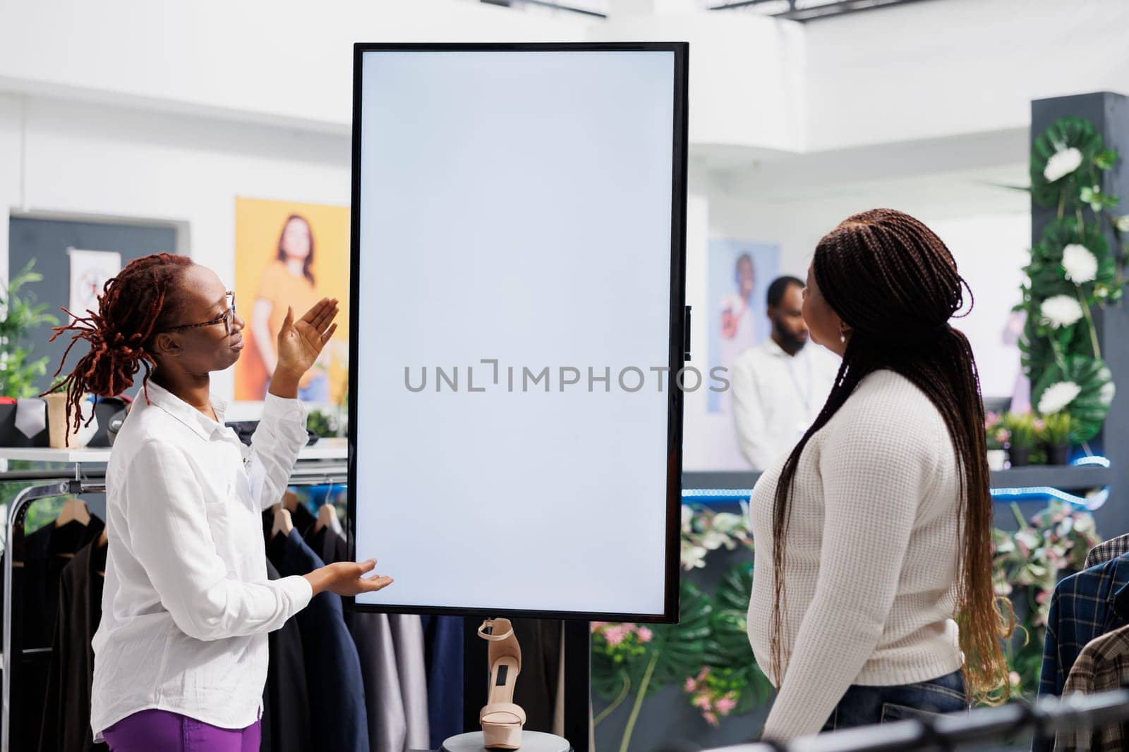 Assistant helping customer choosing shoes, showing style and size options on smart white empty display. Clothing store employee showcasing promotion on blank whiteboard screen mock up