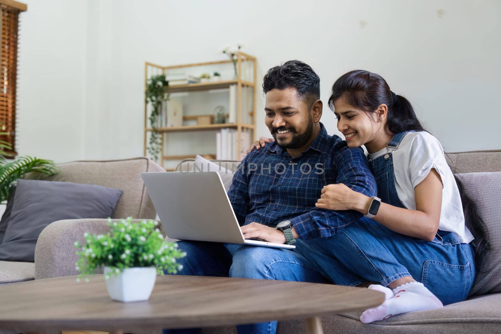 Happy indian Couple Using Laptop Browsing Internet Together on sofa at home.