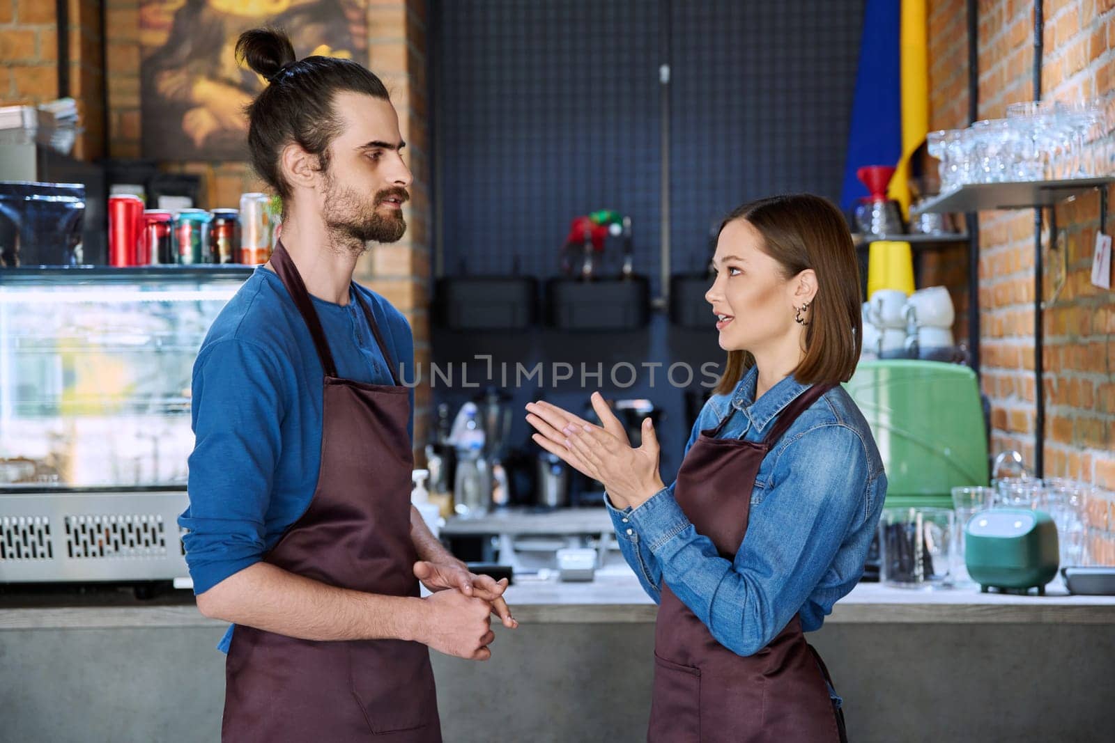 Colleagues business partners young man and woman in aprons talking at workplace by VH-studio