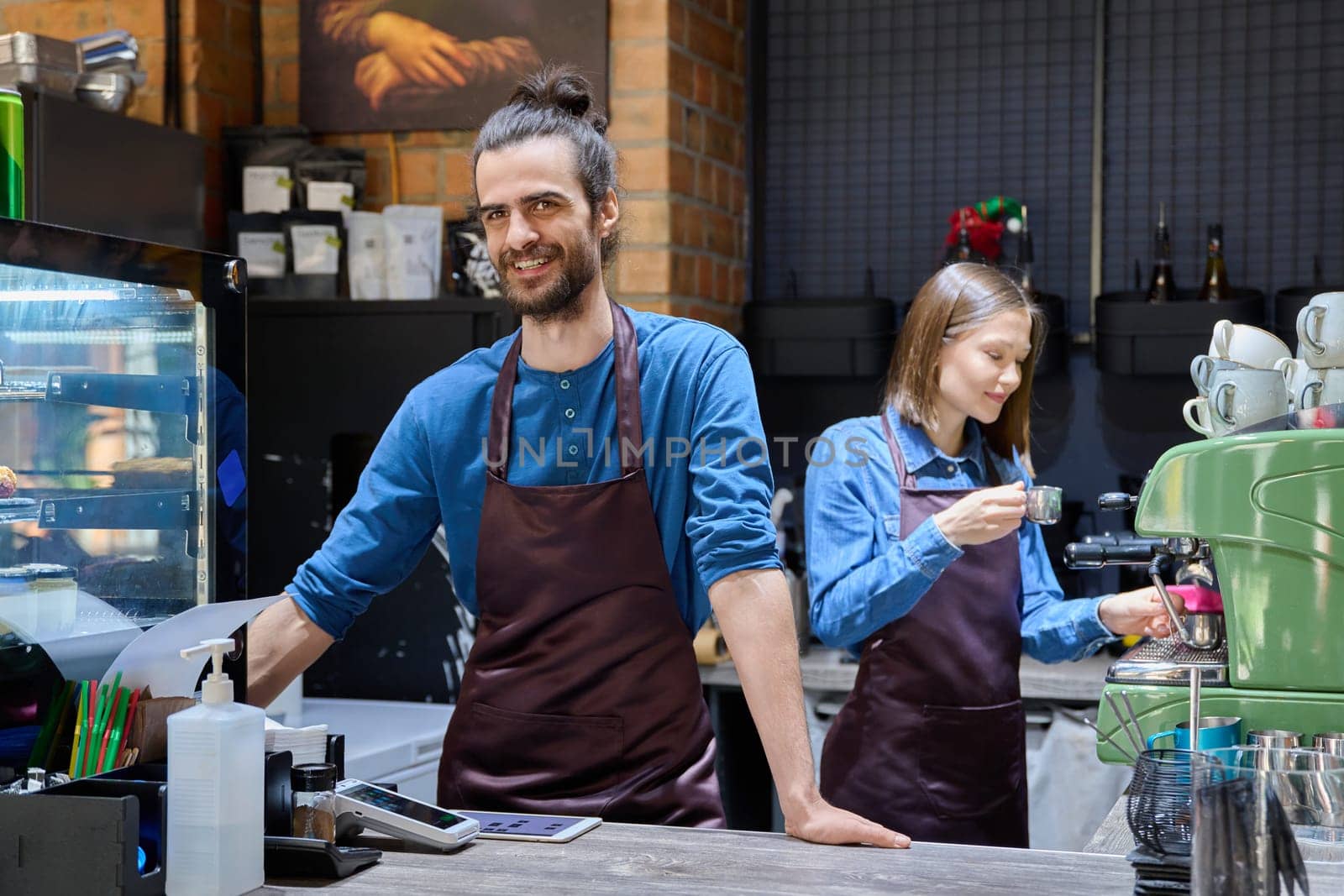 Colleagues partners young man and woman in aprons working together in coffee shop by VH-studio