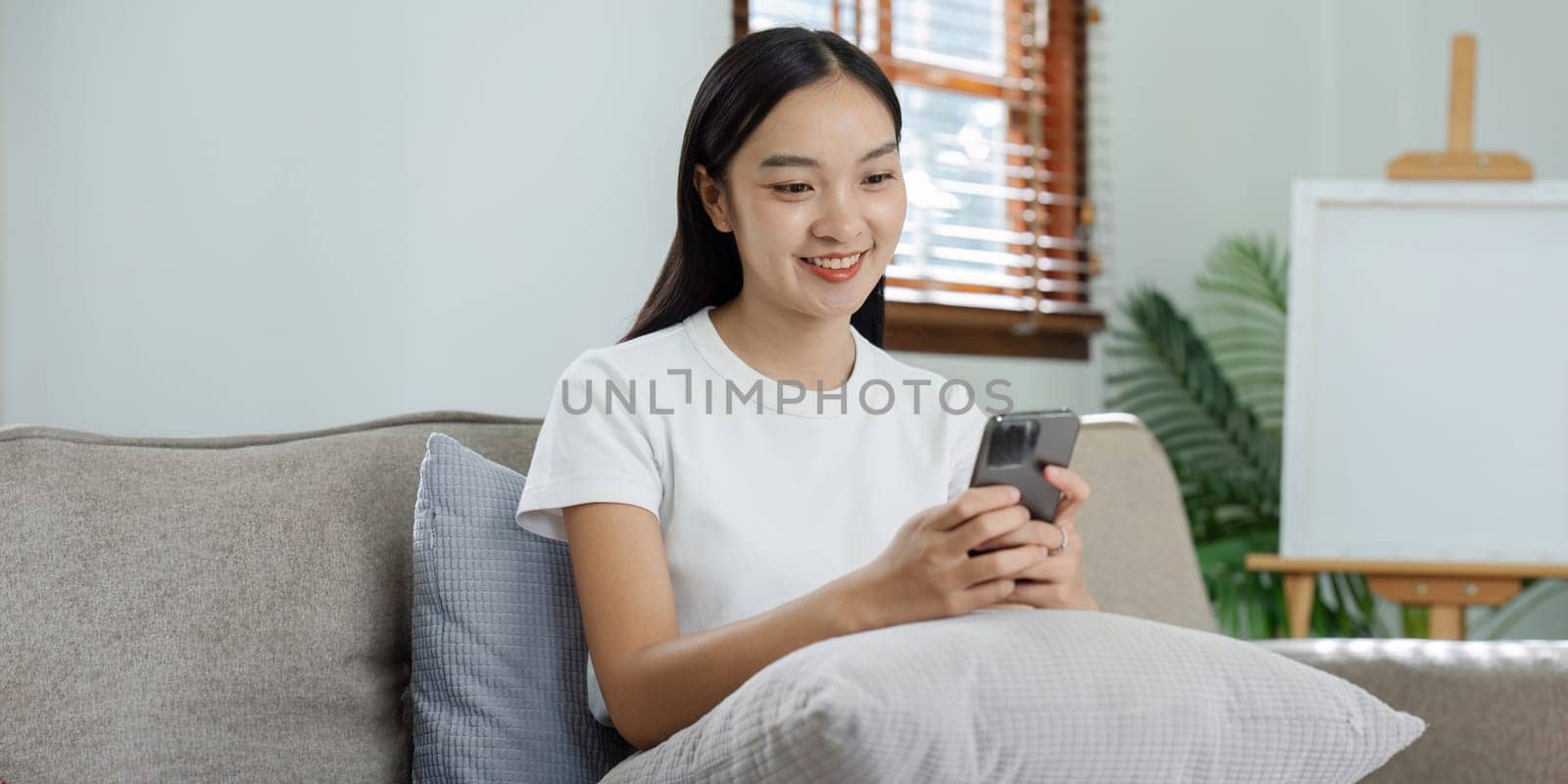 Smiling young Caucasian woman sit relax on couch in living room talk on video call. Happy millennial female rest on sofa at home.