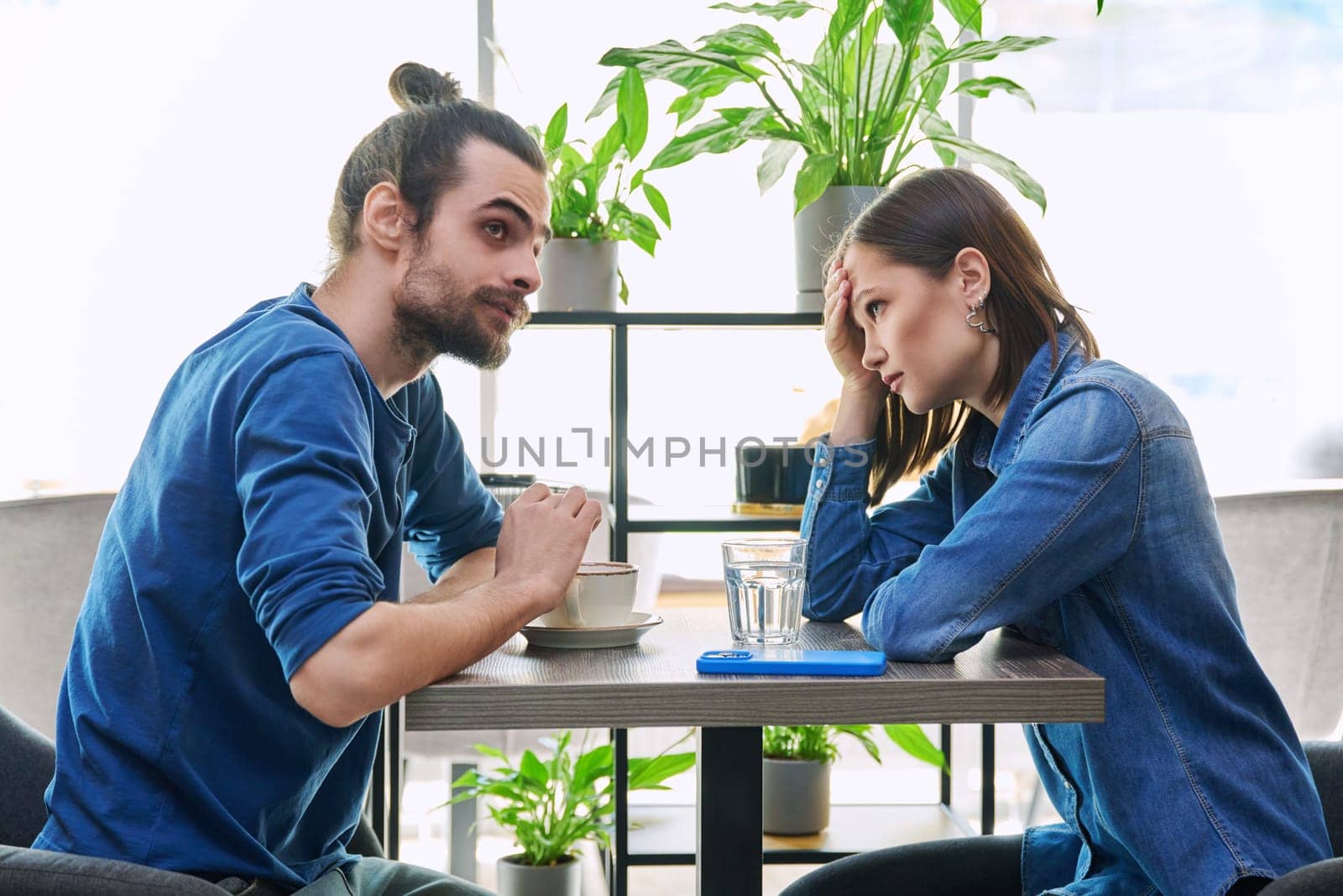 Serious aggressive young couple quarreling, angry, arguing, talking, nervous, sitting together at table in cafeteria. Relationships difficulties problems negative emotions lifestyle people concept