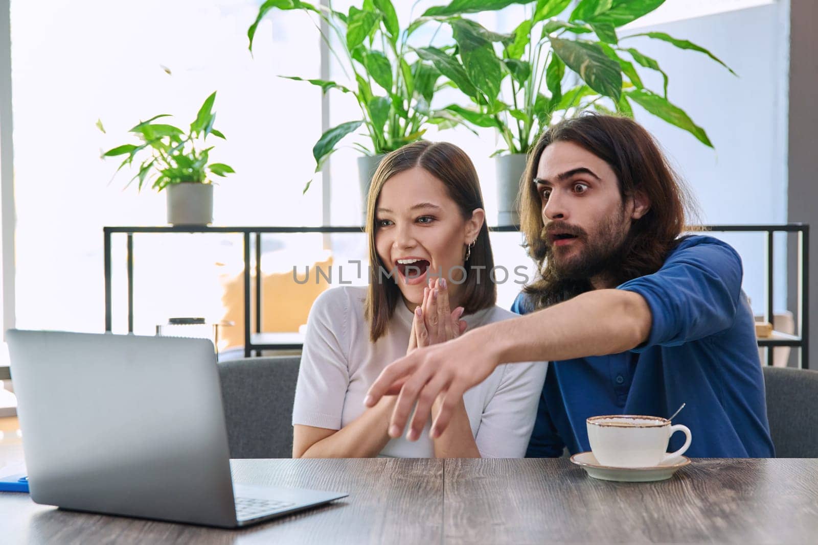 Happy smiling surprised young couple looking at laptop together while sitting in cafe, cafeteria. Leisure time for two, lifestyle, togetherness, relationship, communication, work study remotely