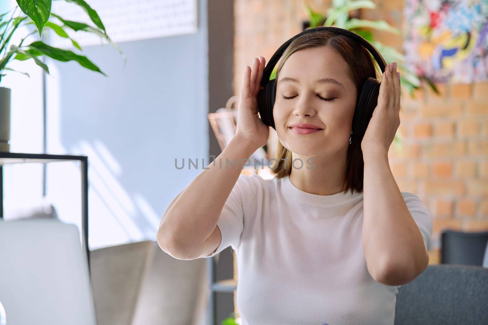 Young happy woman in headphones with closed eyes enjoying music, audio text book. Technology, lifestyle, youth concept