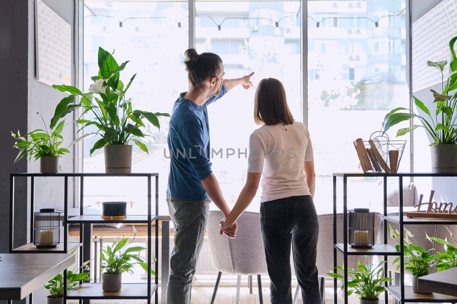 Back view, silhouette of young couple holding hands looking out window. Love friendship romance relationship, happiness, lifestyle, people concept
