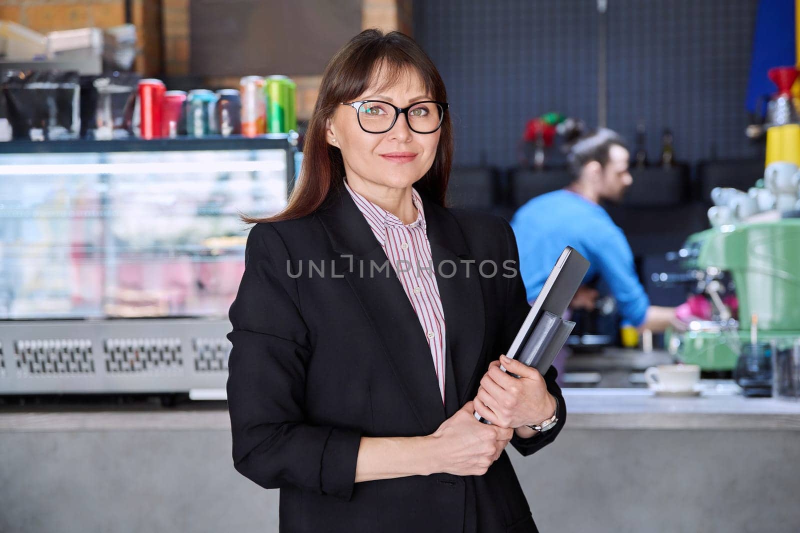 Portrait of confident business woman accountant financier lawyer small business owner. Successful middle-aged female with laptop in hands looking at camera, background coffee shop cafeteria restaurant