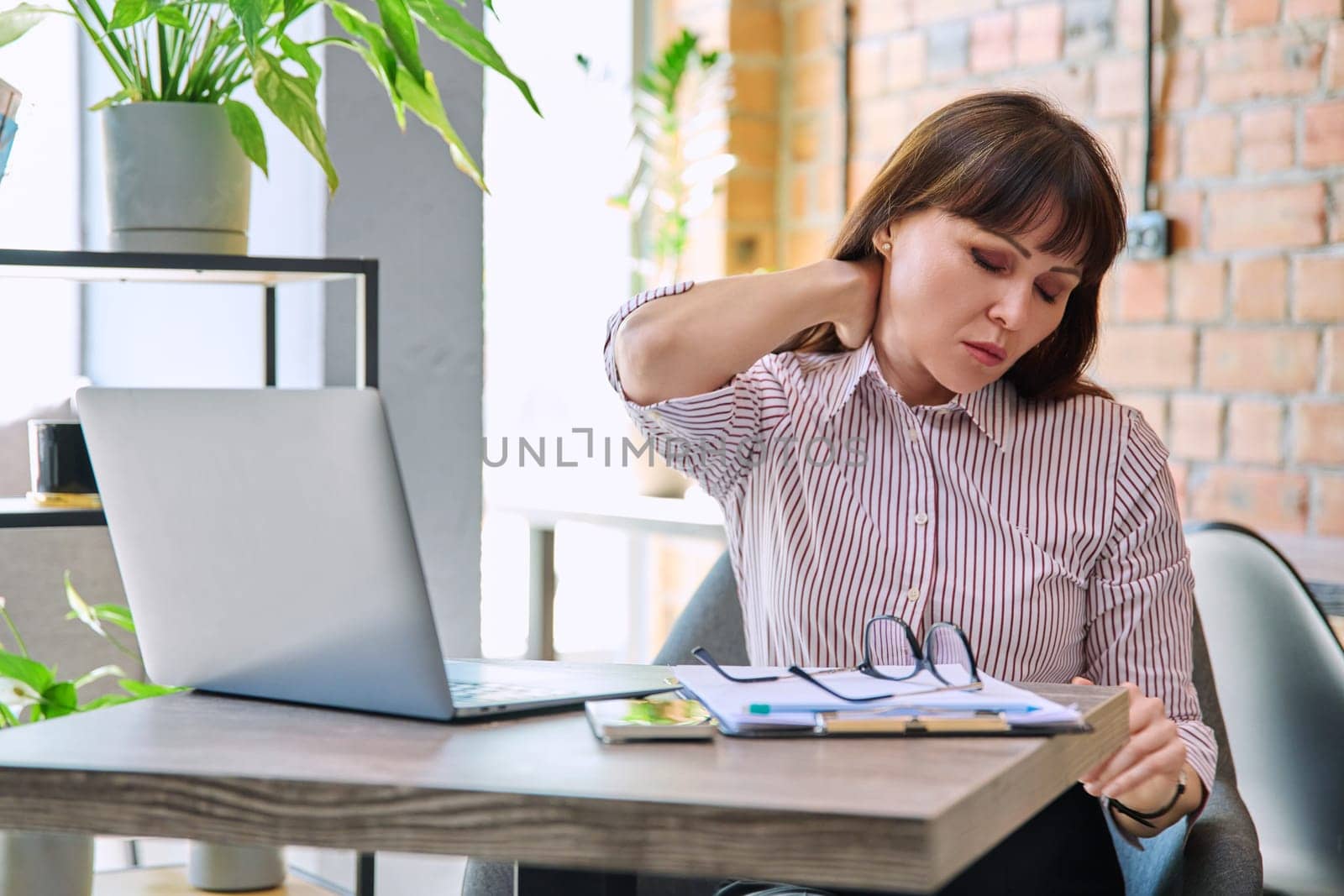 Mature tired worried tense woman at workplace experiencing neck and back pain, stress headache. Health problems older age hormonal diseases mental difficulties migraine depression anxiety pain injury
