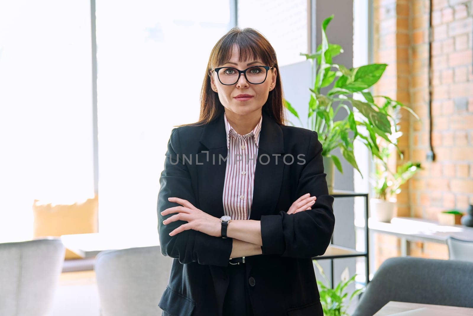 Portrait of a confident mature business woman in a suit looking at the camera. Middle aged elegant serious female director boss with crossed arms. Business, success, reputation, perseverance, honesty