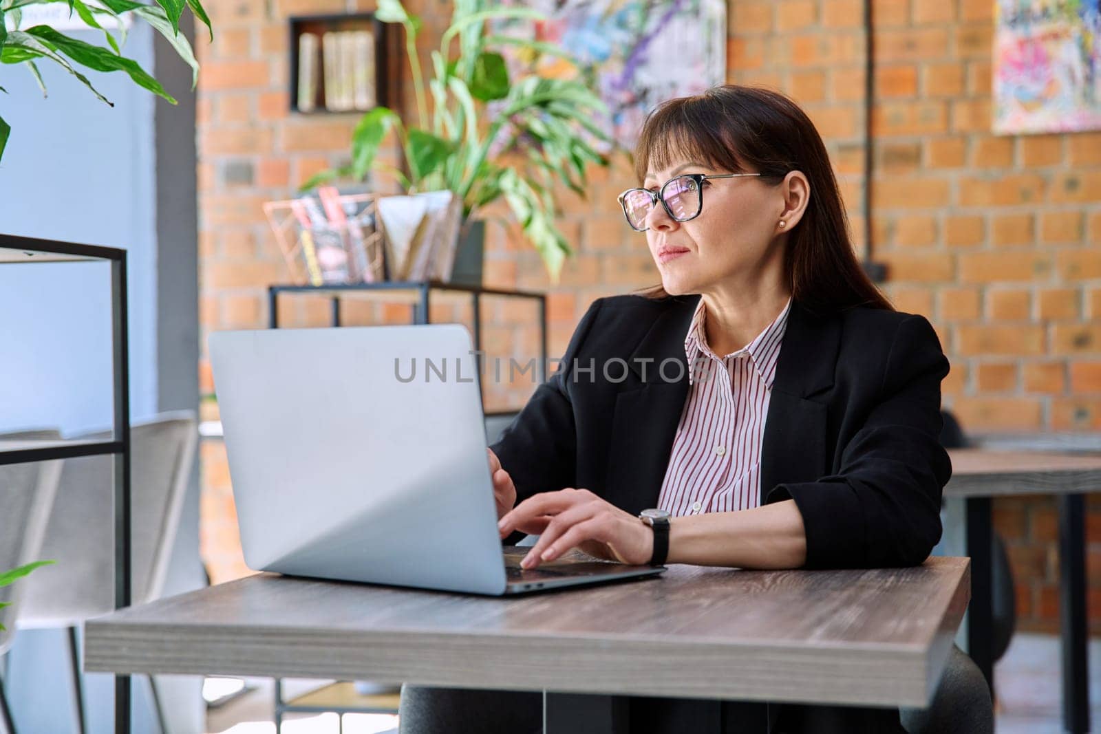 Middle-aged business woman working remotely with laptop in coworking by VH-studio