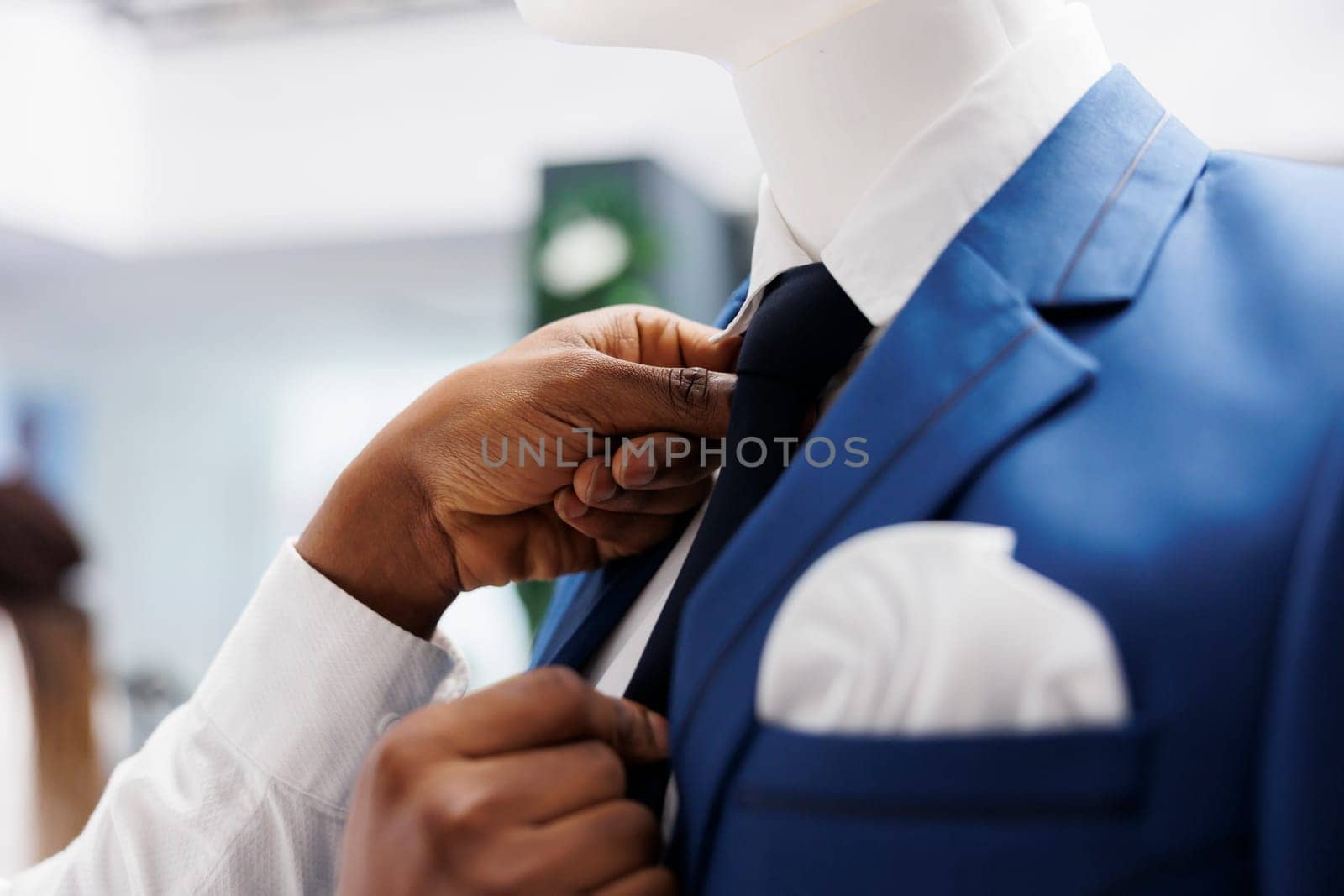 Fashion boutique stylist hands fixing tie and creating formal look on mannequin. African american arms dressing model in suit to display menswear brand in department shopping mall