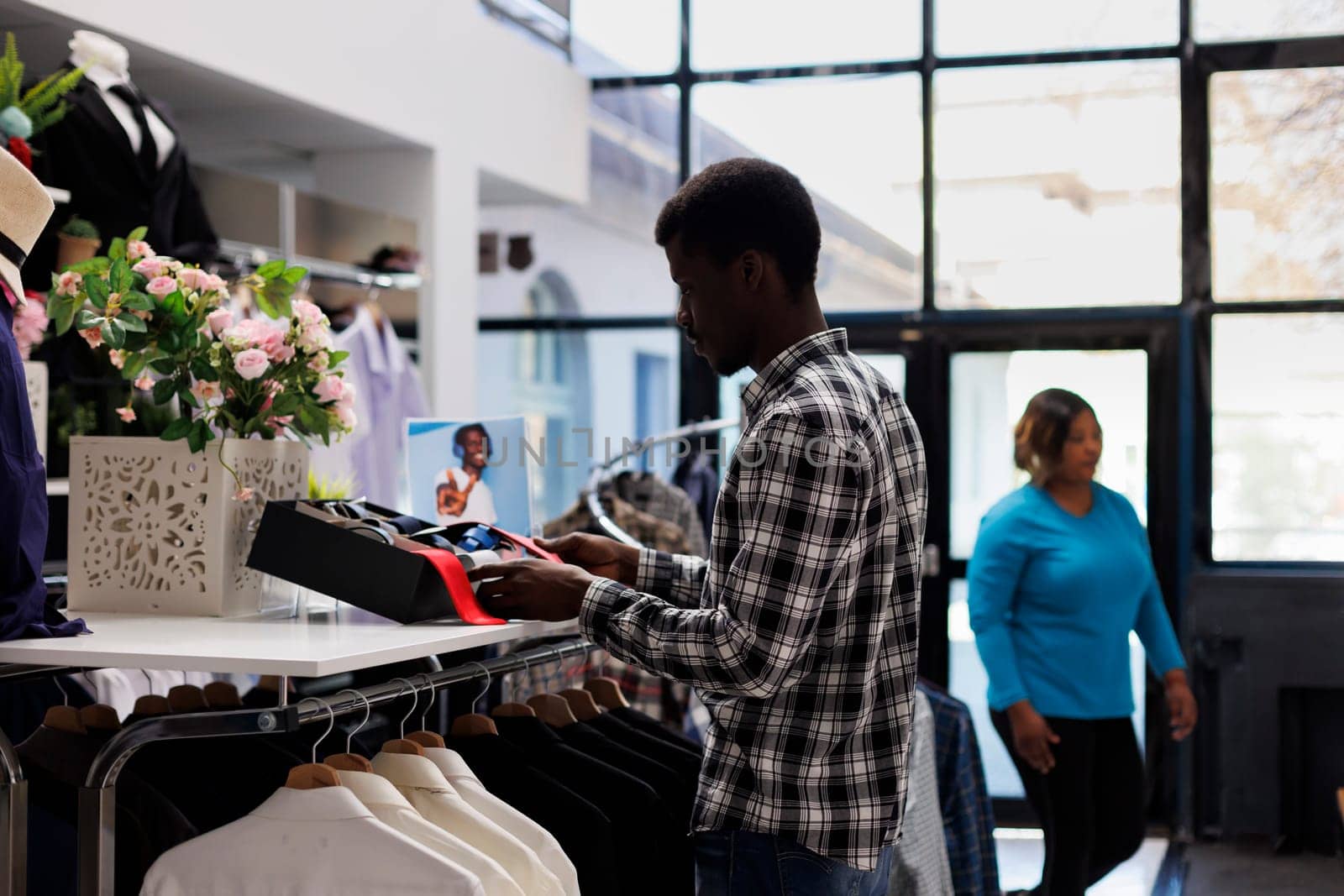 African american customer looking at shelf full with accessories, checking fashionable belt in modern boutique. Stylish man shopping for casual wear in clothing store. Fashion concept